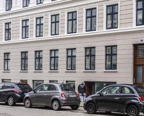 Bygning med grå facade og parkerede biler ved gadeplan