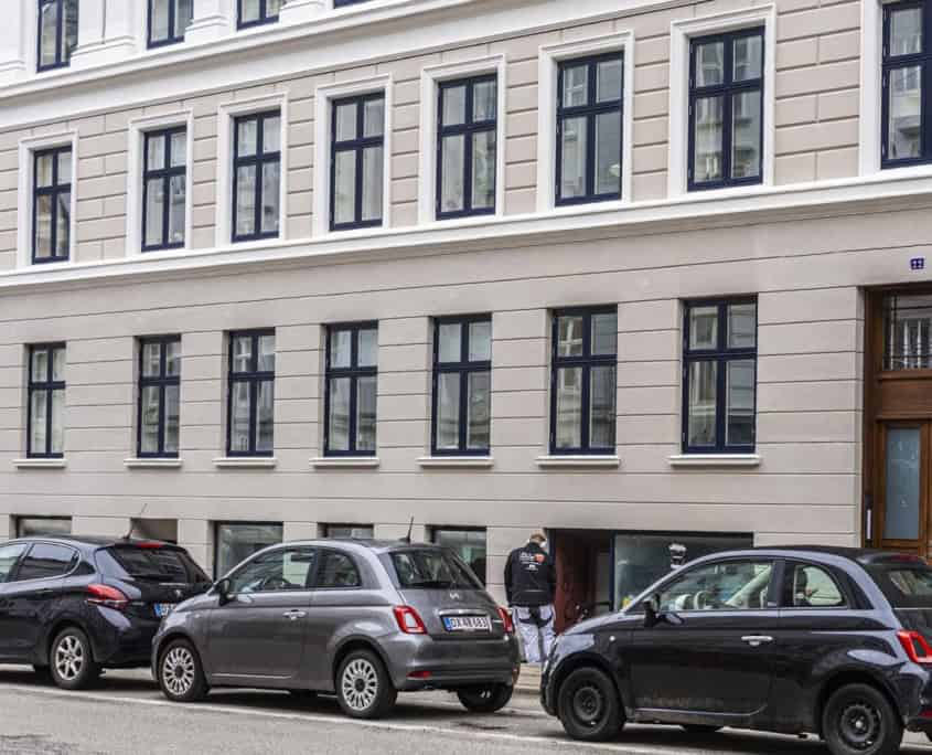 Bygning med grå facade og parkerede biler ved gadeplan